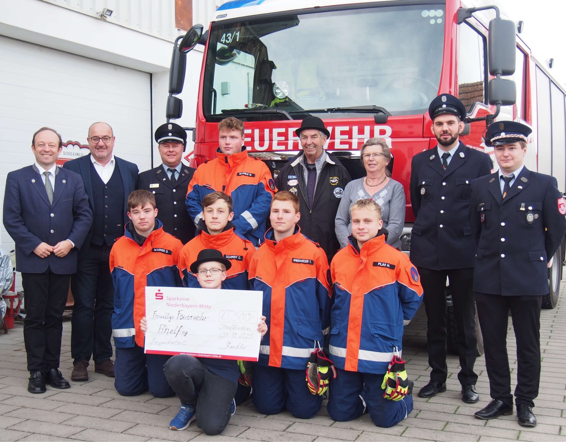 Foto FFW-Jugend-Aholfing.jpg: Die Familie Kandler übergab einen Spendenscheck in Höhe von 500 Euro für die Aholfinger Jugendfeuerwehr: Alfred Kandler (4. von rechts) , Rosemarie Kandler (3. von rechts), Joschua Seidel (1. Reihe mit Scheck) und die Führungsriege der Feuerwehr mit Ehrengästen
